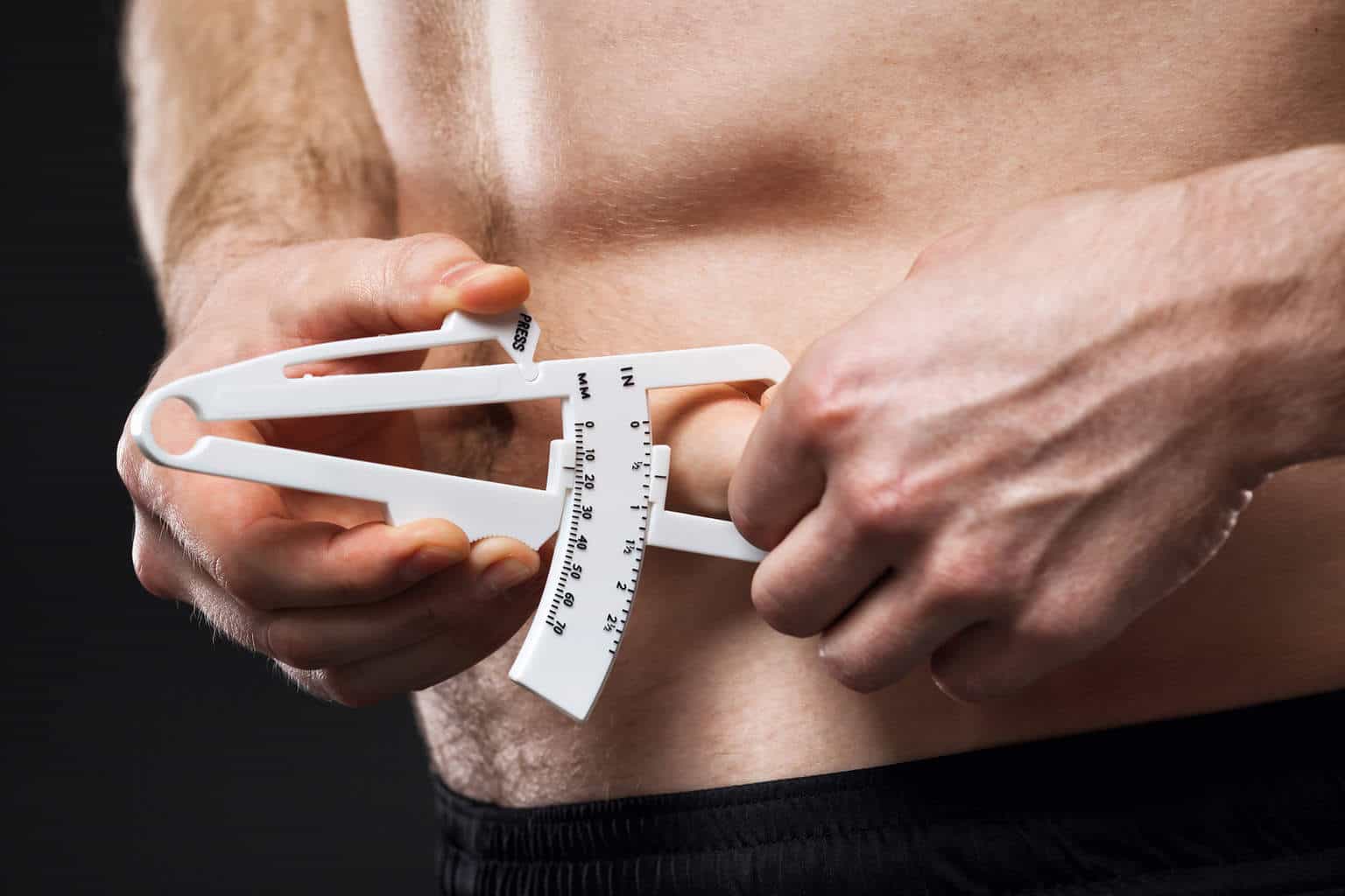 Young man is measuring his body fat with calipers.