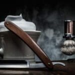 Shaving razors and bowl with foam on wooden background