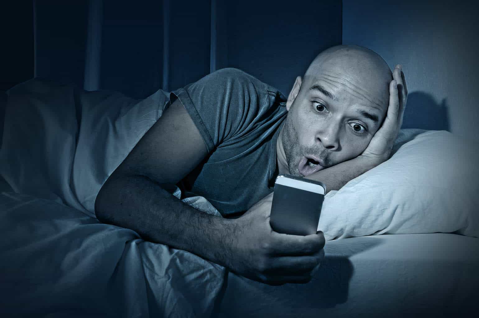 Young Cell Phone Addict Man Awake At Night In Bed Using Smartpho