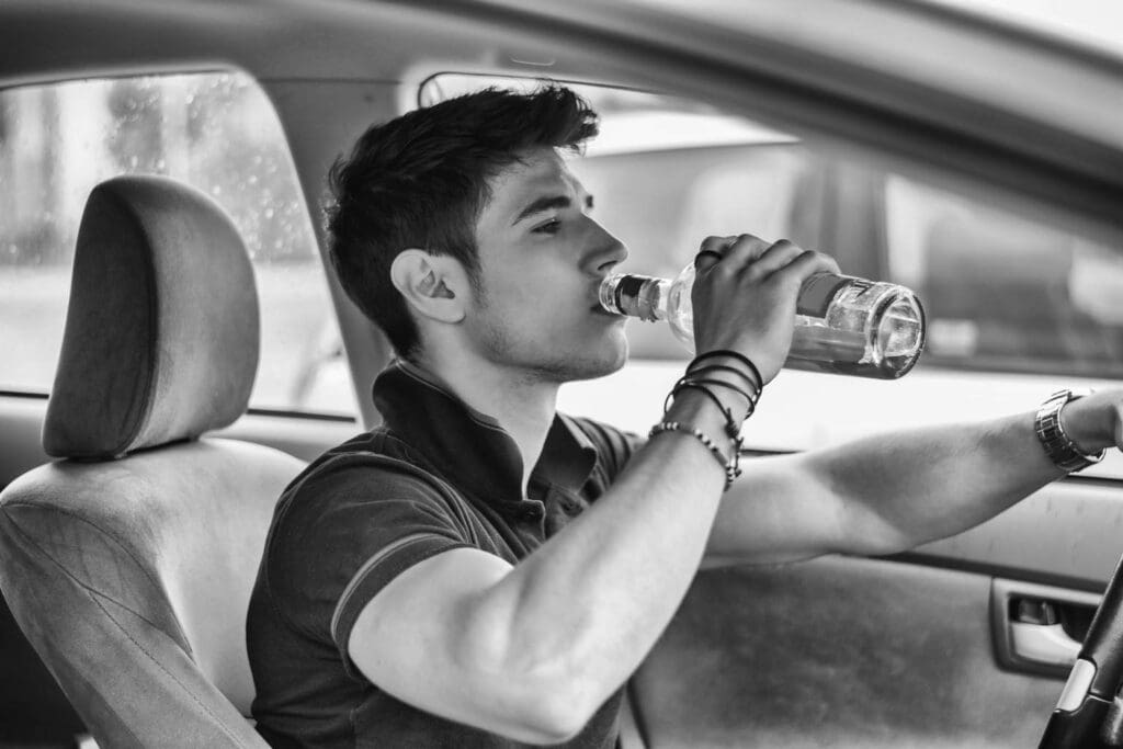 Young man driving his car while drinking alcohol