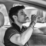 Young man driving his car while drinking alcohol