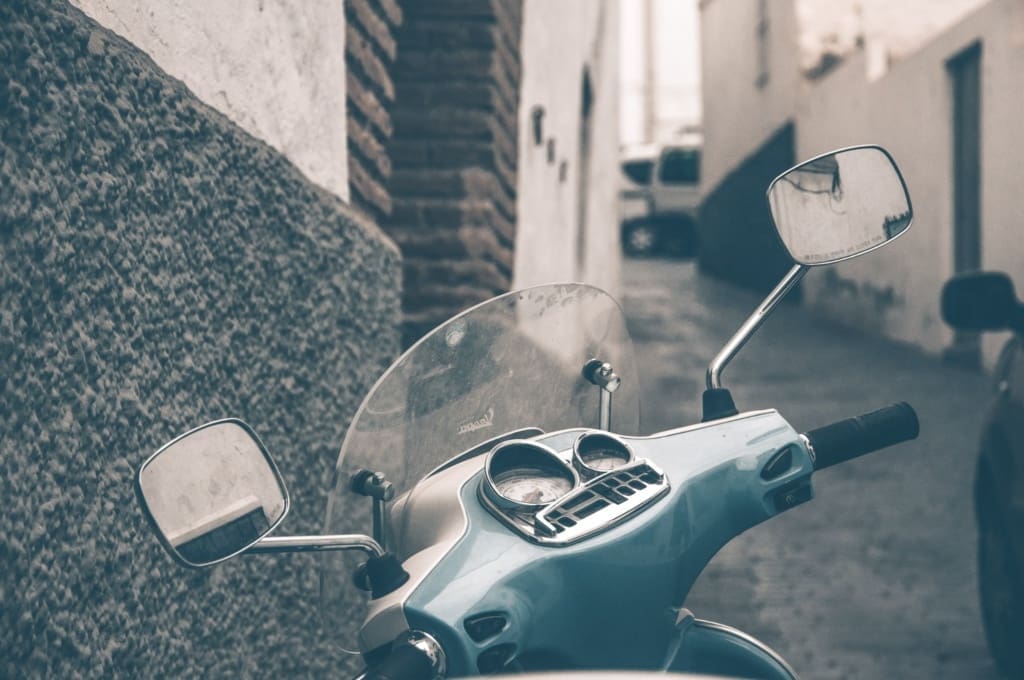 Vintage scooter met windscherm geparkeerd in een smalle steeg.