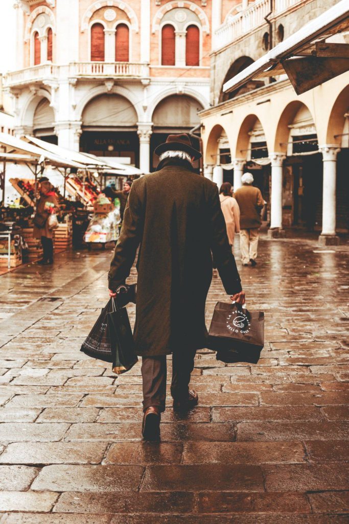 stijlvolle oudere man loopt door Europese straat met shopping tassen en klassieke architectuur