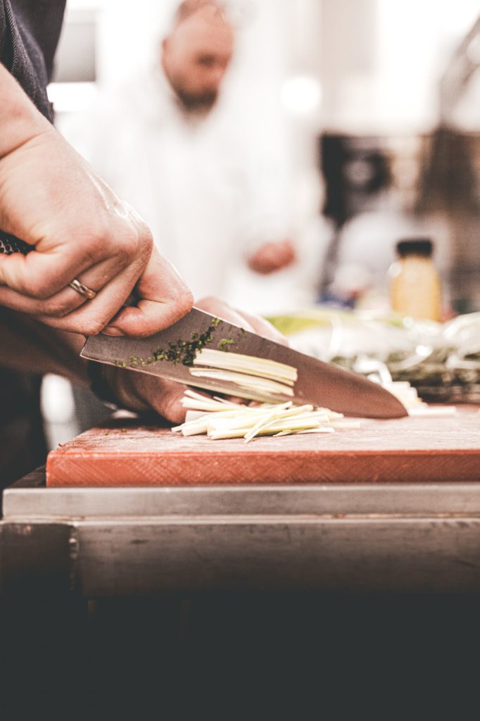 Close-up van een chef die verse ingrediënten fijnsnijdt op een houten snijplank.